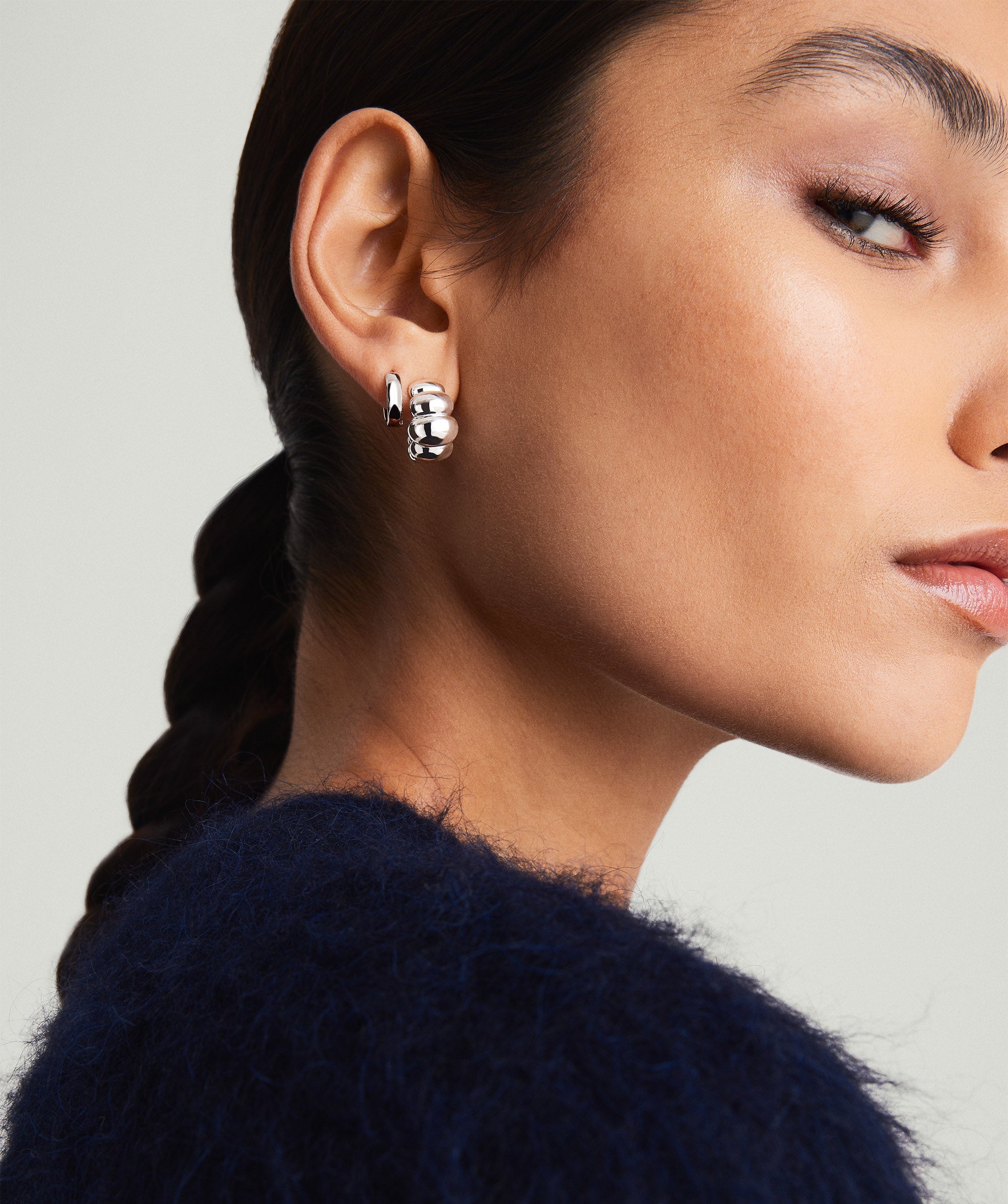 Close-up of a woman wearing Puffy Charlotte Hoops earrings, showcasing their bold, silver design from the Charlotte Collection.