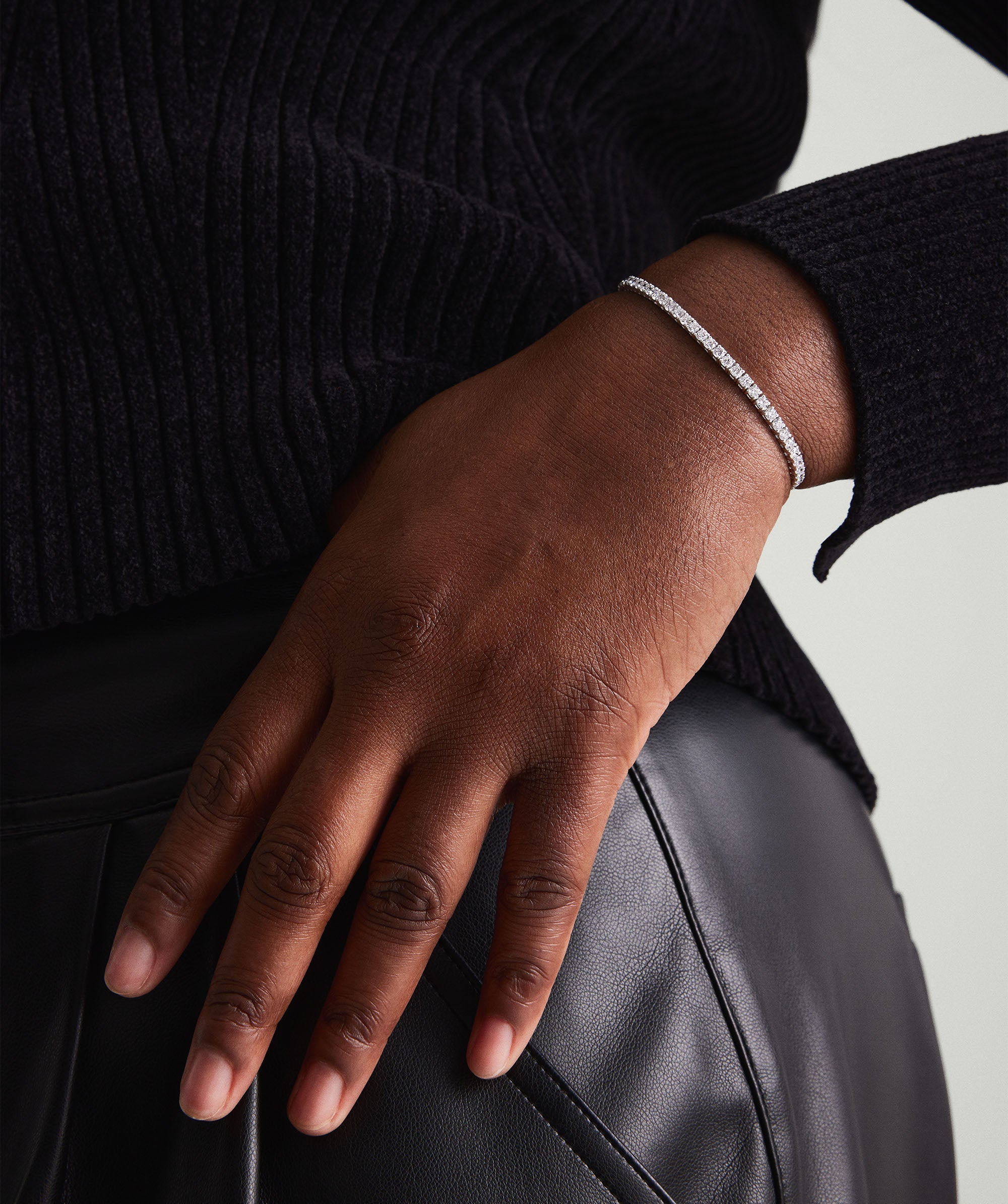 Hand wearing the Lab Grown Diamond Tennis Bracelet 2.5mm on black leather pants, highlighting the bracelet's sparkle and craftsmanship.