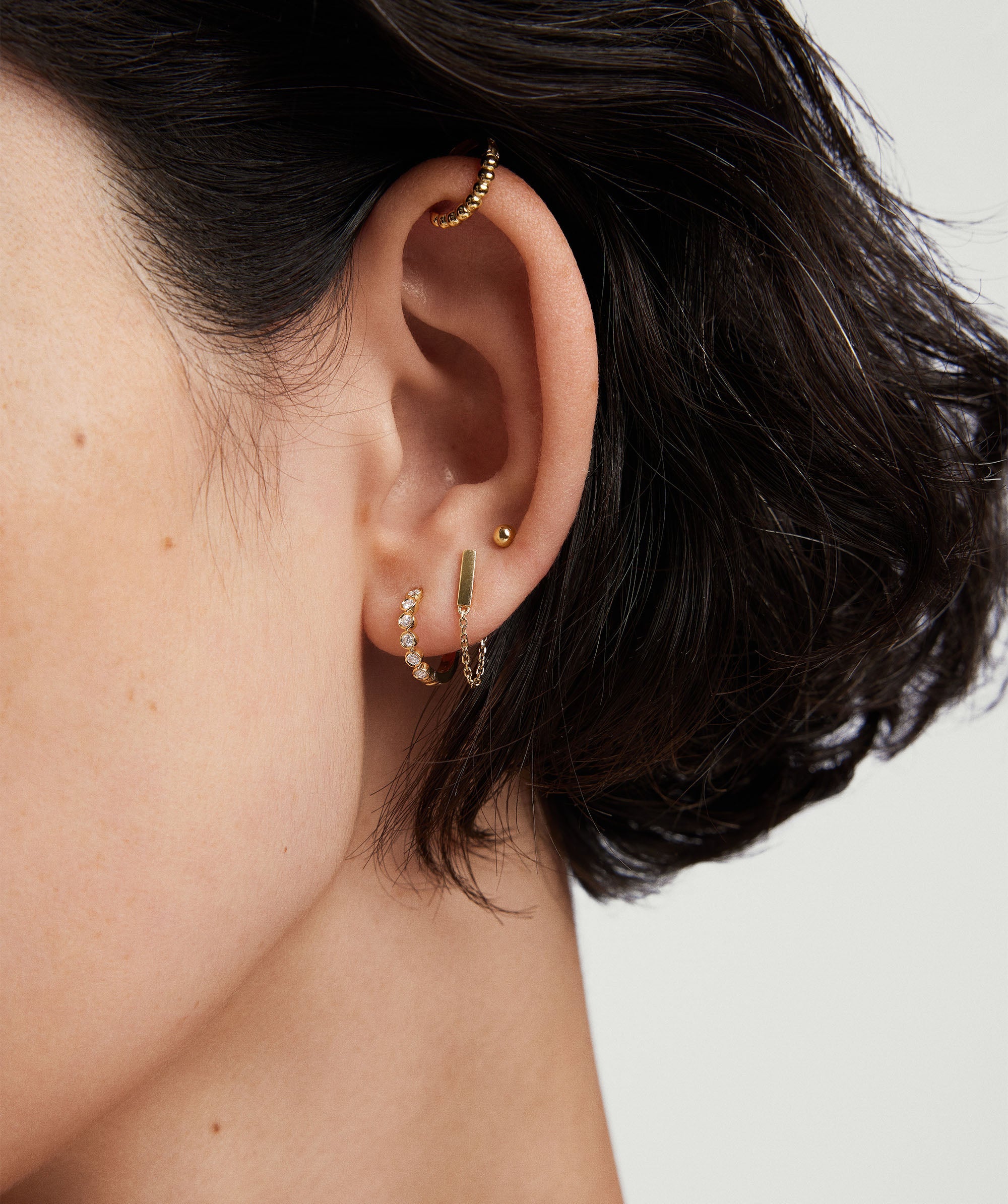 Close-up of a woman's ear adorned with Bezel Lab Grown Diamond Huggies in 14k solid gold, featuring sparkling, ethically produced lab grown diamonds.