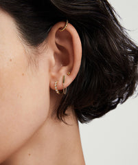 Close-up of a woman's ear adorned with Bezel Lab Grown Diamond Huggies in 14k solid gold, featuring sparkling, ethically produced lab grown diamonds.