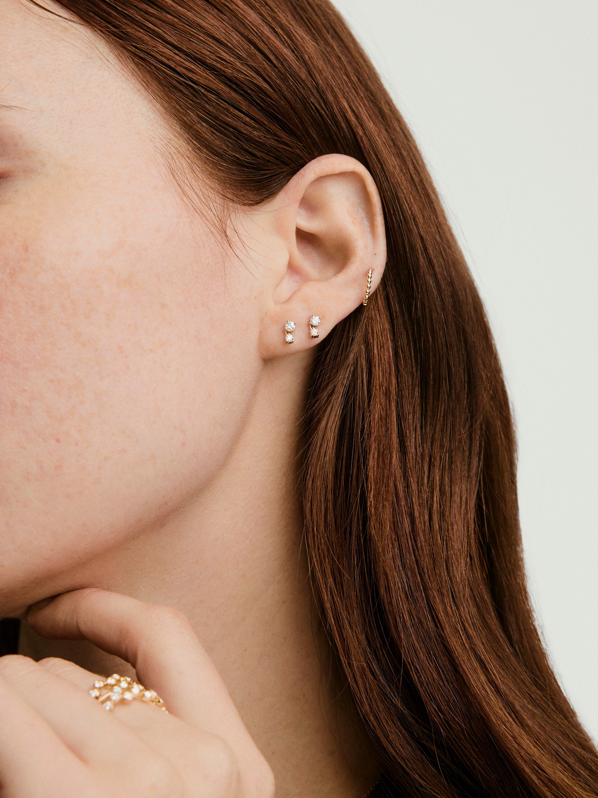 Close-up of a woman's ear adorned with droplet-style lab grown diamond stud earrings, designed to move and reflect light, highlighting their elegance.