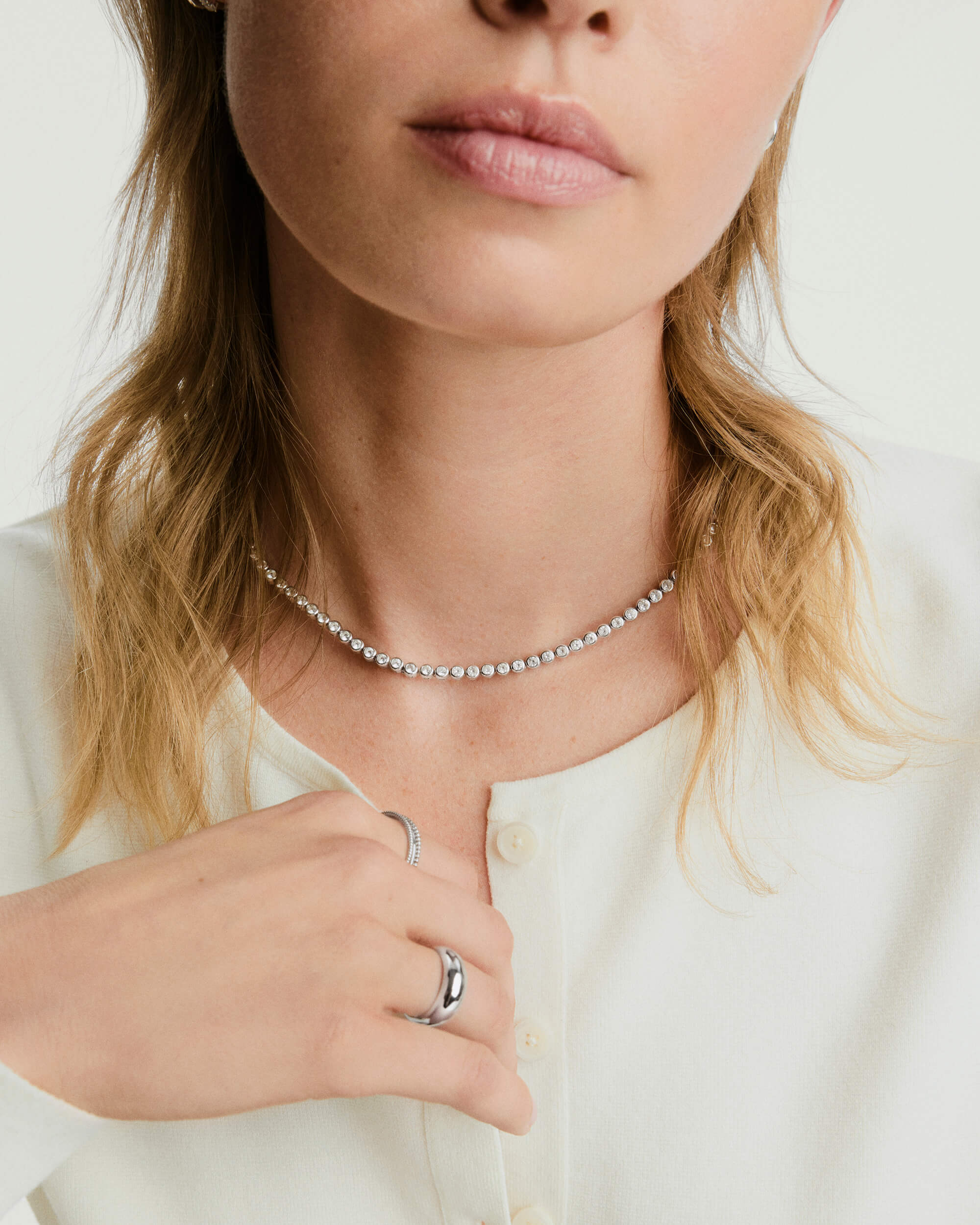 A woman showcases the Zadie Bezel Lab Grown Sapphire Tennis Necklace, elegantly draped around her neck, highlighting its sophisticated bezel setting design.