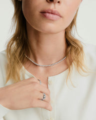A woman showcases the Zadie Bezel Lab Grown Sapphire Tennis Necklace, elegantly draped around her neck, highlighting its sophisticated bezel setting design.