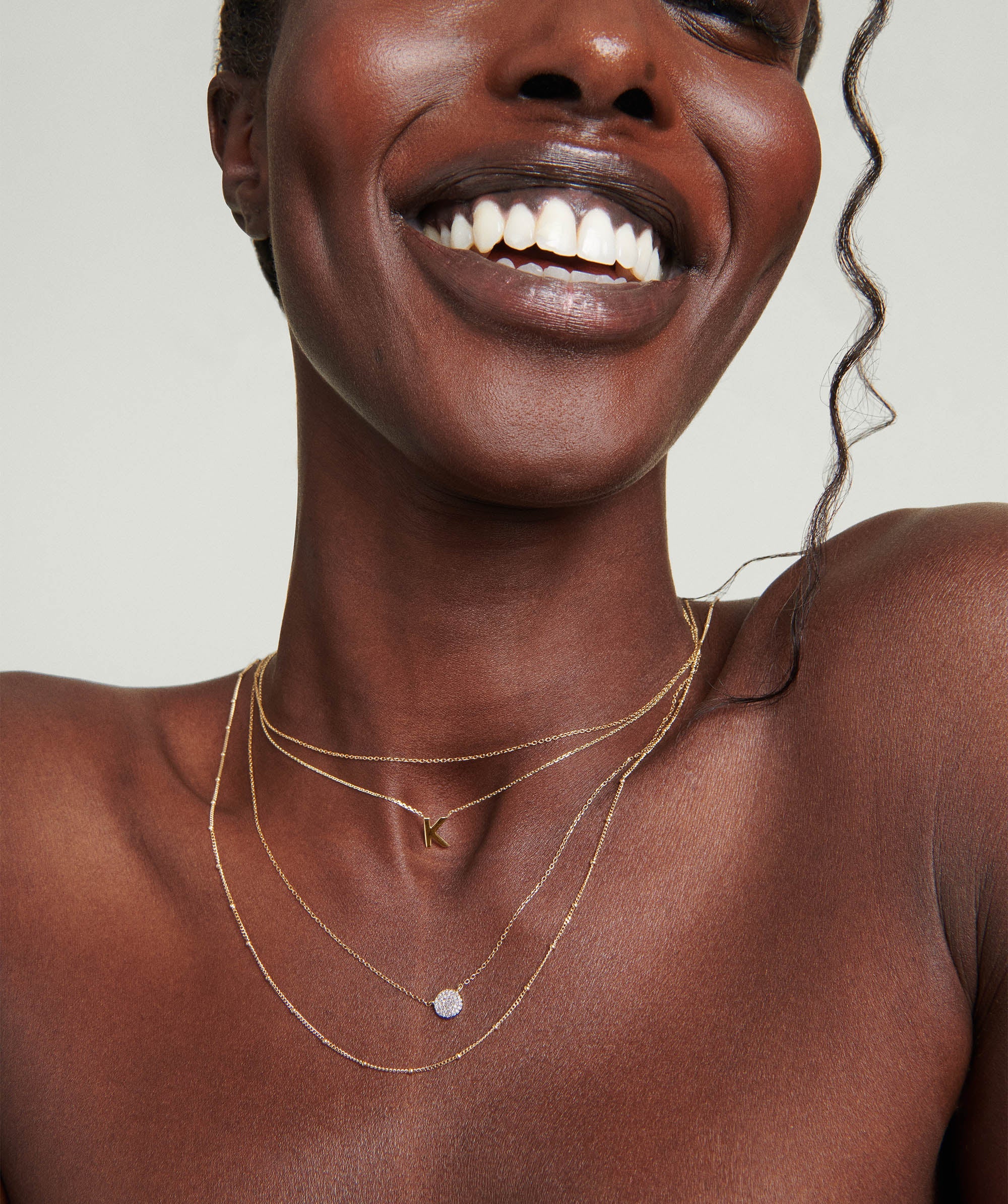 Woman smiling, showcasing the Large PavÃ© Diamond Round Necklace. The handcrafted 14k gold necklace features a stunning array of responsibly sourced diamonds.