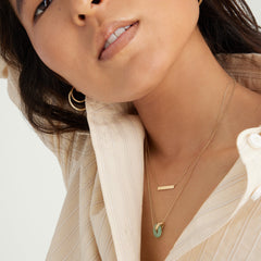 Woman wearing the Linked Gemstone Necklace with gold interlinked rings and a green aventurine link, posing for a portrait.
