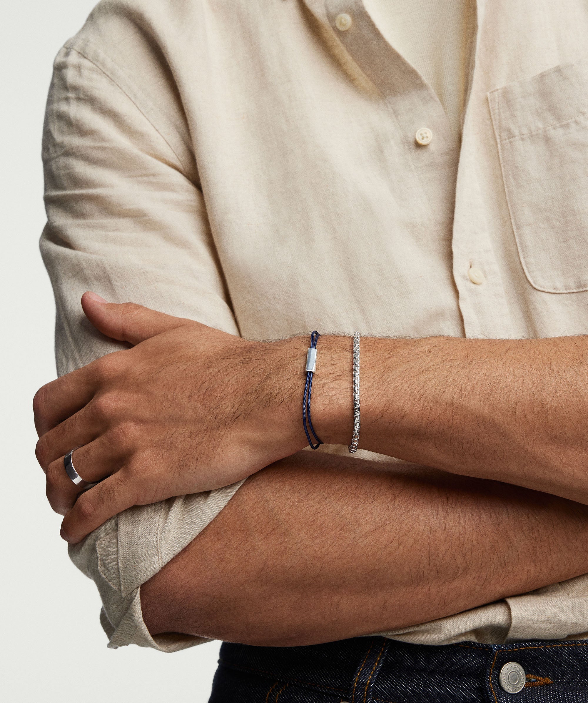 Man wearing a white shirt and blue jeans, displaying a silver Bar Cord Bracelet on his wrist.