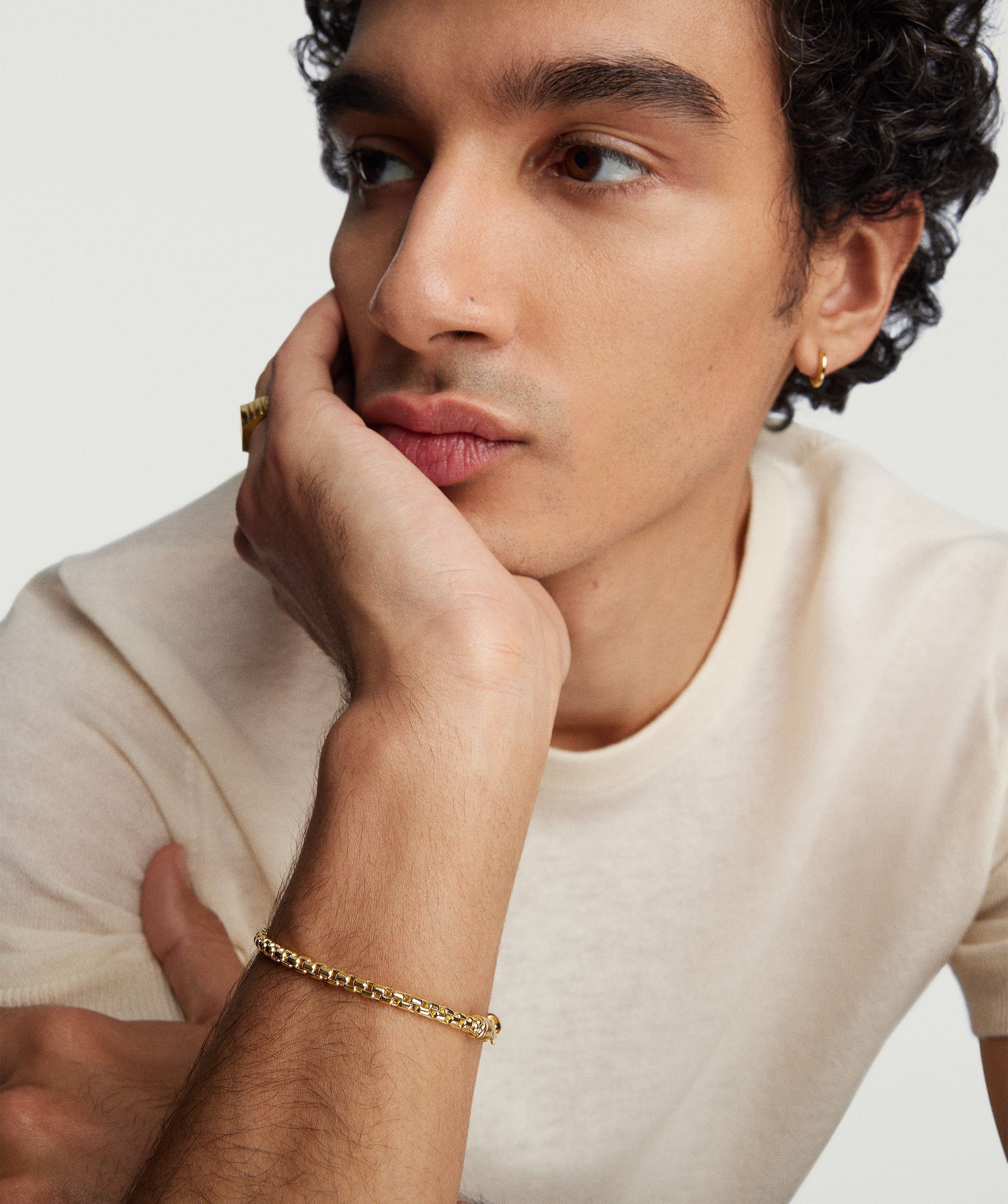Man with curly hair wearing a white shirt showcases the 3mm Round Box Chain Bracelet, handcrafted in 14k solid yellow gold.
