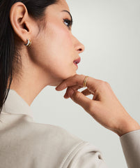 Woman wearing Duet Mixed Huggie Hoops, showcasing dual metal earrings in 18k gold vermeil and sterling silver, with hand on chin.