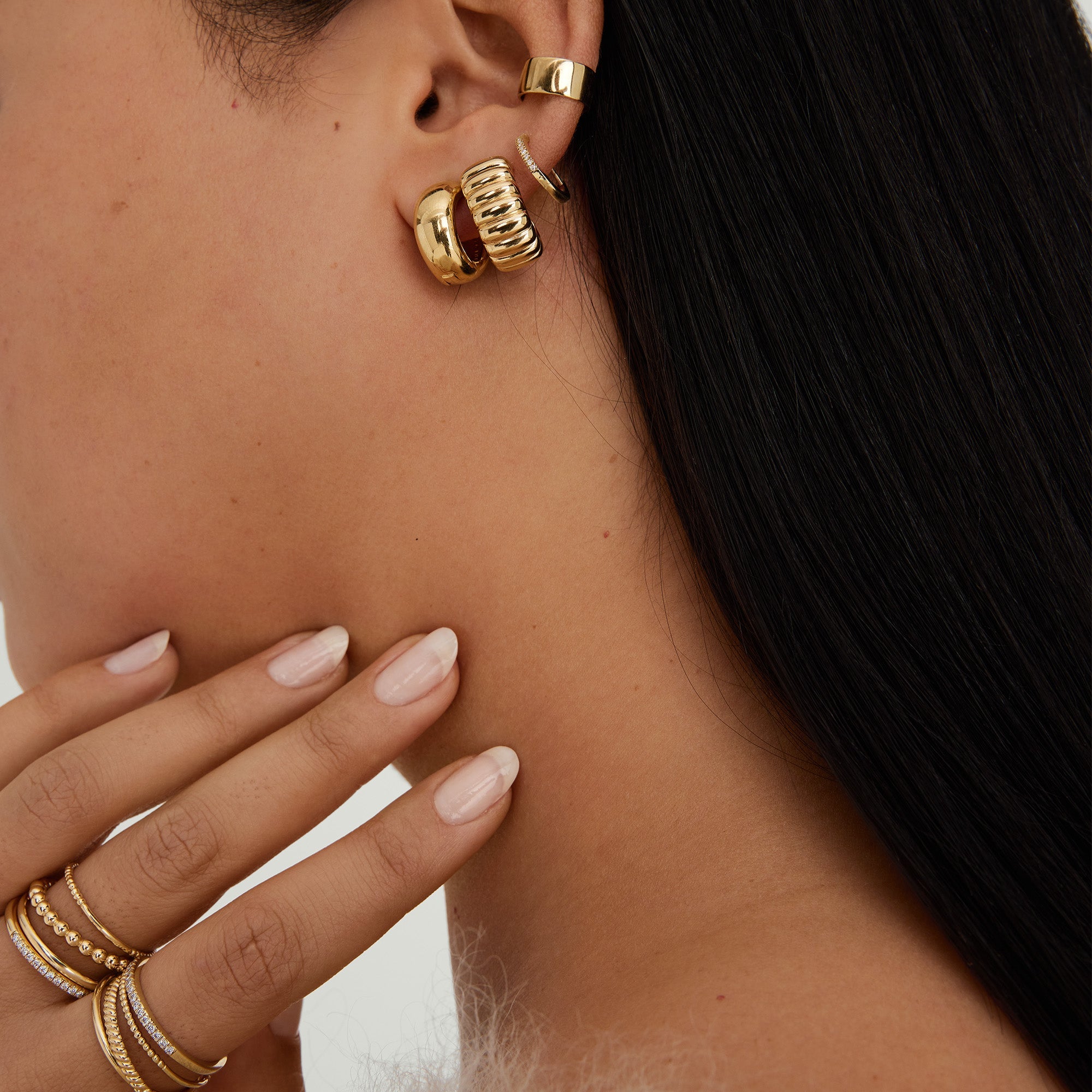 Woman wearing Chunky Medium Hoops, featuring clicker closure for comfort. Close-up shows gold earrings stacked stylishly, highlighting their pillowy design.