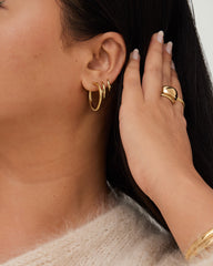 Woman wearing Tube Hoops Bundle, featuring Huggie, Medium, and Large Hoops. Close-up of gold earrings and ring on hand, showcasing fine jewelry.