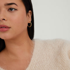 Woman wearing Tube Large Hoops, gold hoop earrings with a clicker closure, styled with a white sweater. Close-up highlights the earring's bold and lightweight design.