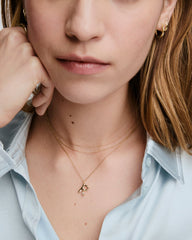 Close-up of a woman wearing the Organic DÃ´me Liquid Letter Pendant Necklace, featuring a unique gold hand gesture pendant with gemstone accents.