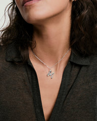 Woman wearing an Organic DÃ´me Liquid Letter Pendant, featuring a silver pendant with a gemstone, resting elegantly on her neck.