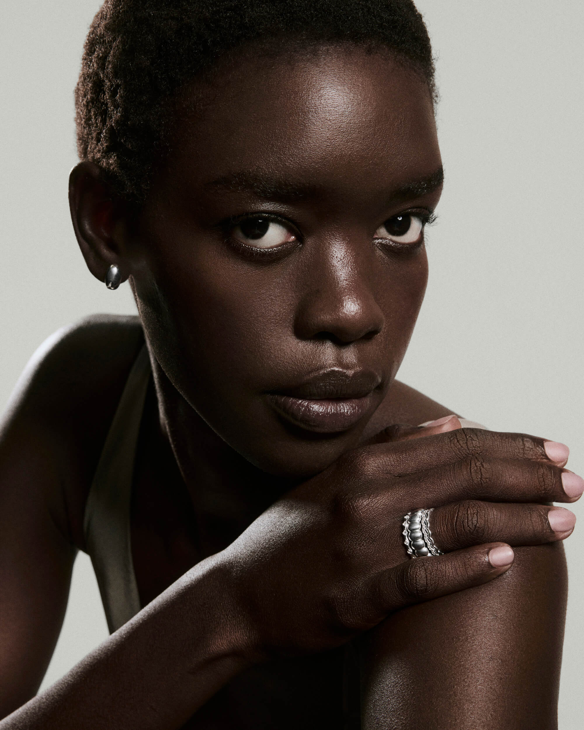 Dark-skinned woman wearing the Charlotte Crest Stacker Ring, featuring curved edges and delicate sapphires, with silver hoop earring, hand resting on shoulder.