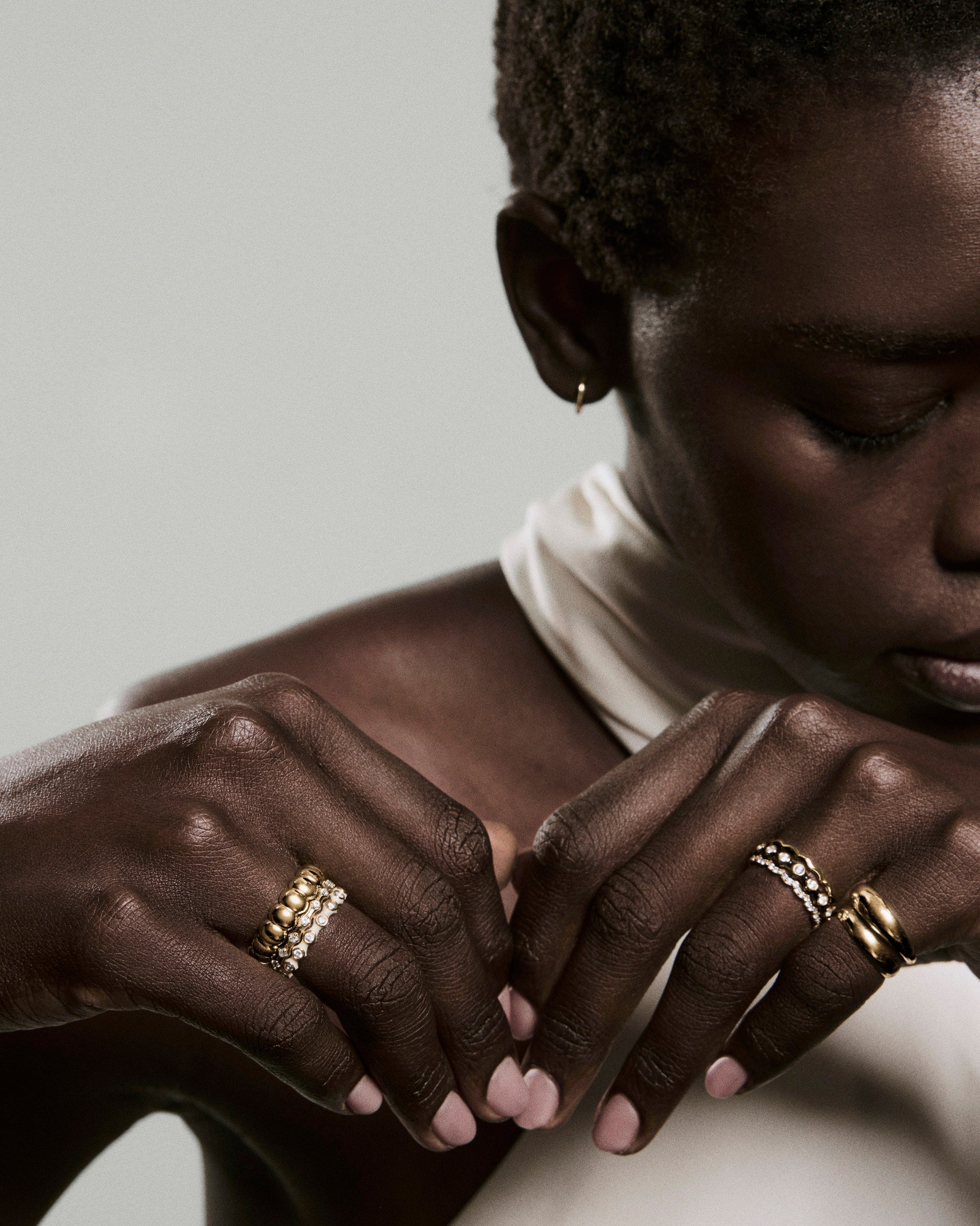 Person's hands adorned with multiple rings, including the Enamel Charlotte Stacker Ring, featuring clean enamel edges and bezel-set lab-grown sapphires, highlighting elegant, stackable jewelry.