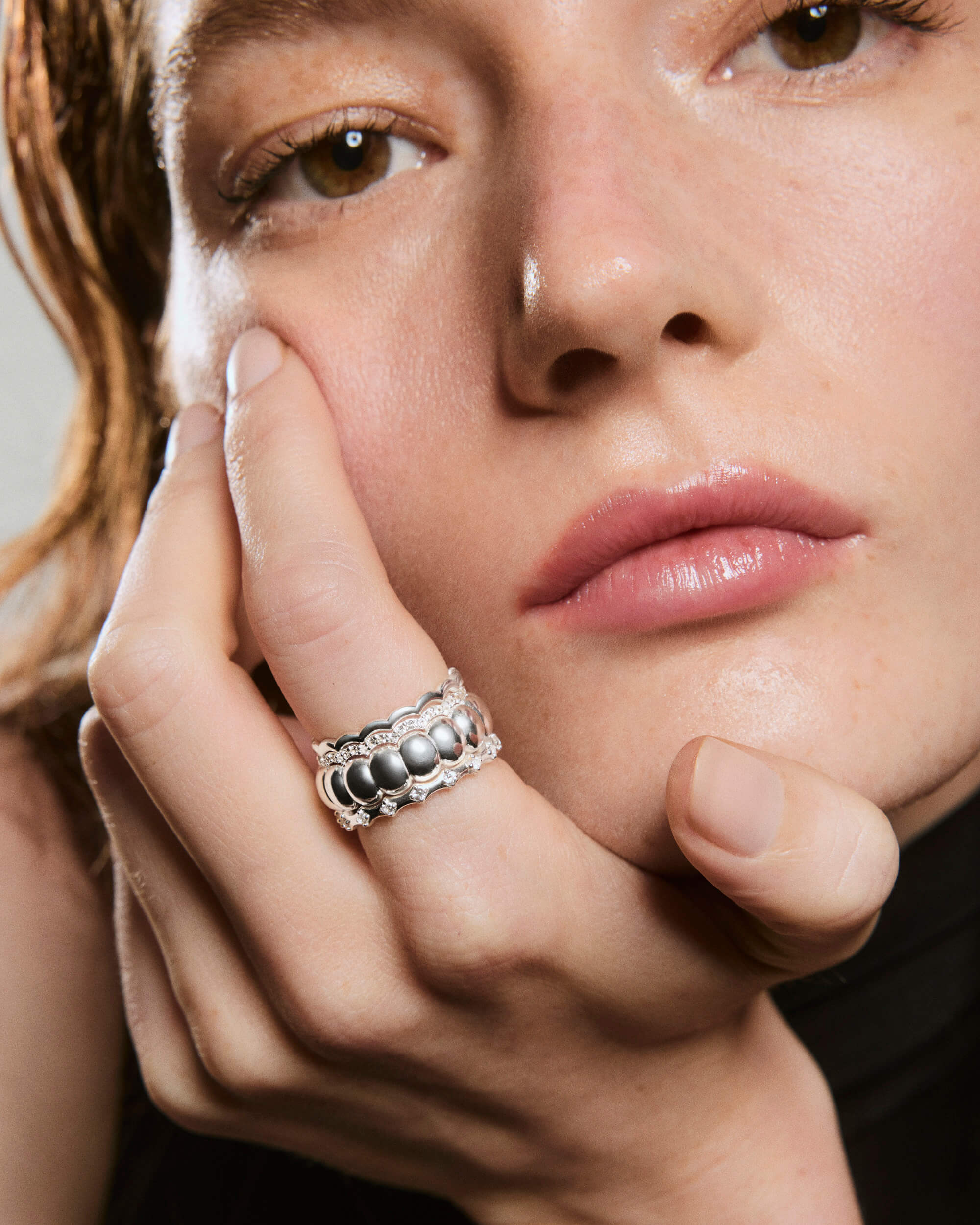 Close-up of a hand resting on a face, wearing the Puffy Charlotte Stacker Ring with smooth silver beads and a scalloped, stone-encrusted design.