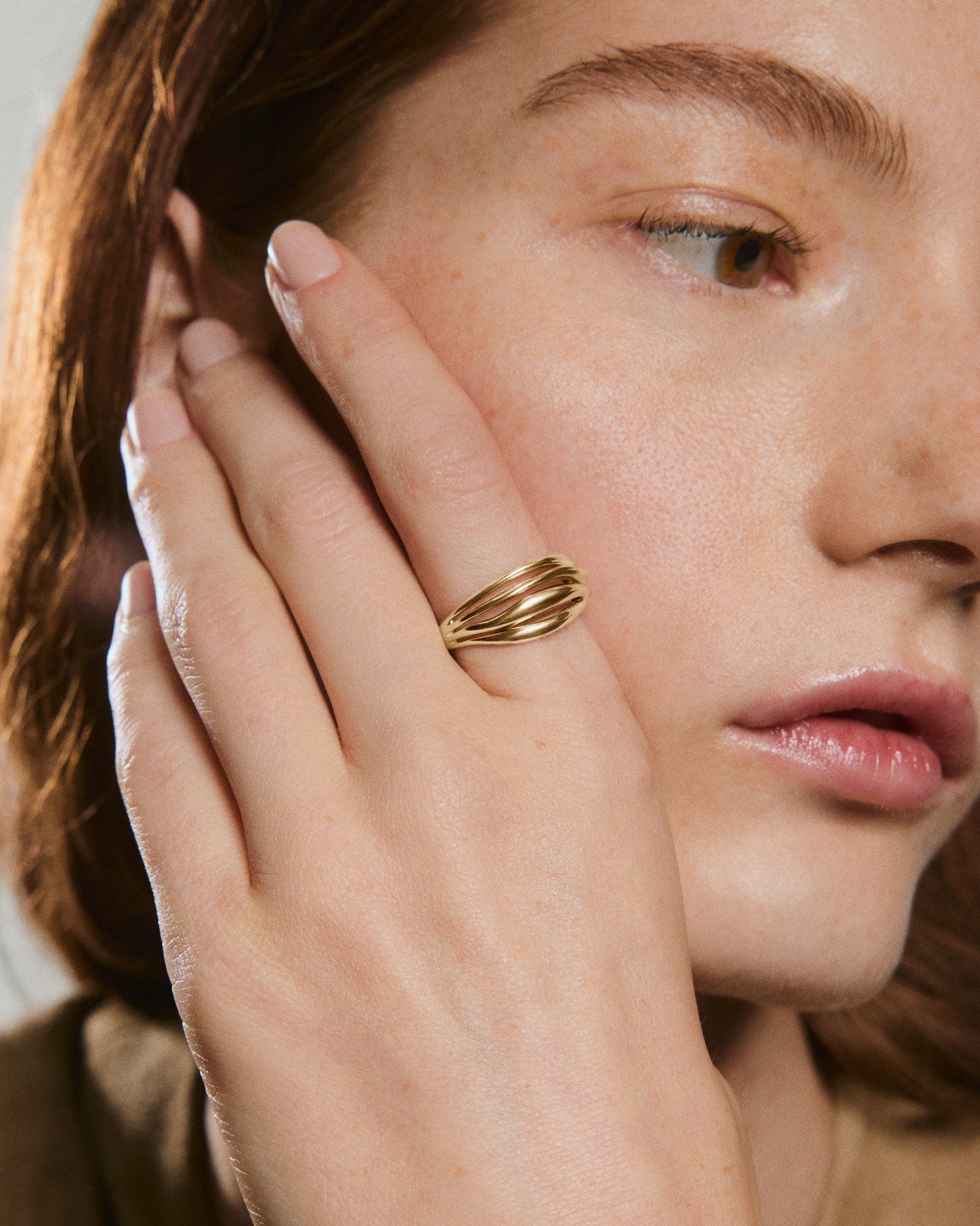 Close-up of a face highlighting the Bold Open DÃ´me Ring on a manicured hand, showcasing its elegant, intertwined gold bands and understated design.