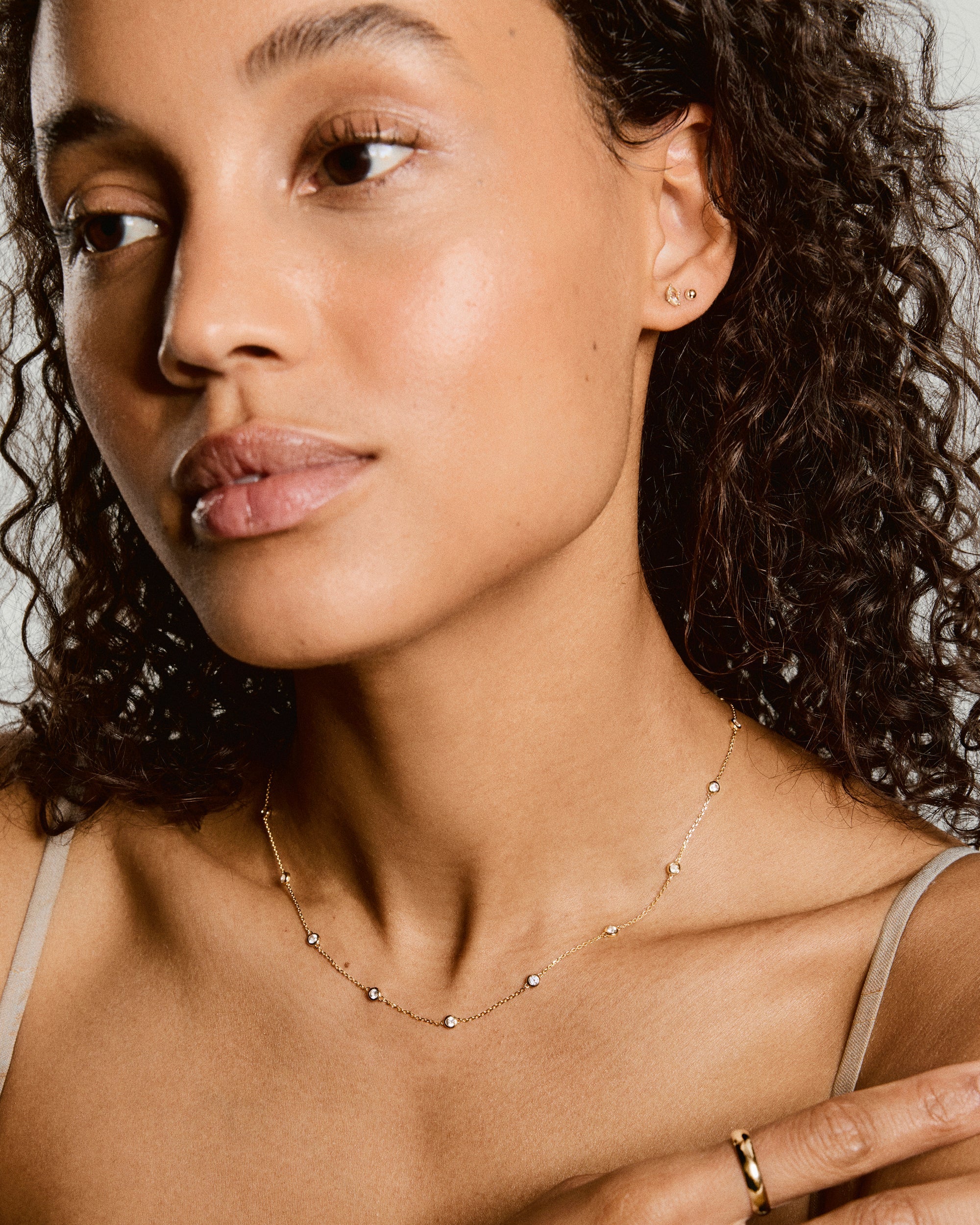 Young woman wearing the Lab Grown Sapphire Orbit Necklace, featuring tiny white stones on a delicate gold chain, complementing her minimalistic gold earrings and ring.