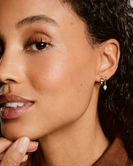 Woman wearing Bia Mini Hoops: one plain gold hoop and one with a dangling teardrop lab-grown sapphire, highlighting her smooth skin and manicured nails.