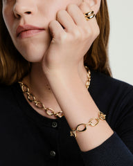 Woman wearing Organic DÃ´me Ripple Chain Bracelet, featuring open, organic shapes linked with a toggle clasp, alongside a matching gold necklace.