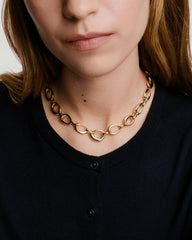 A woman wears the Organic DÃ´me Ripple Chain Necklace featuring organic, irregular links and a toggle clasp, highlighting its elegant, fluid design on her neck.