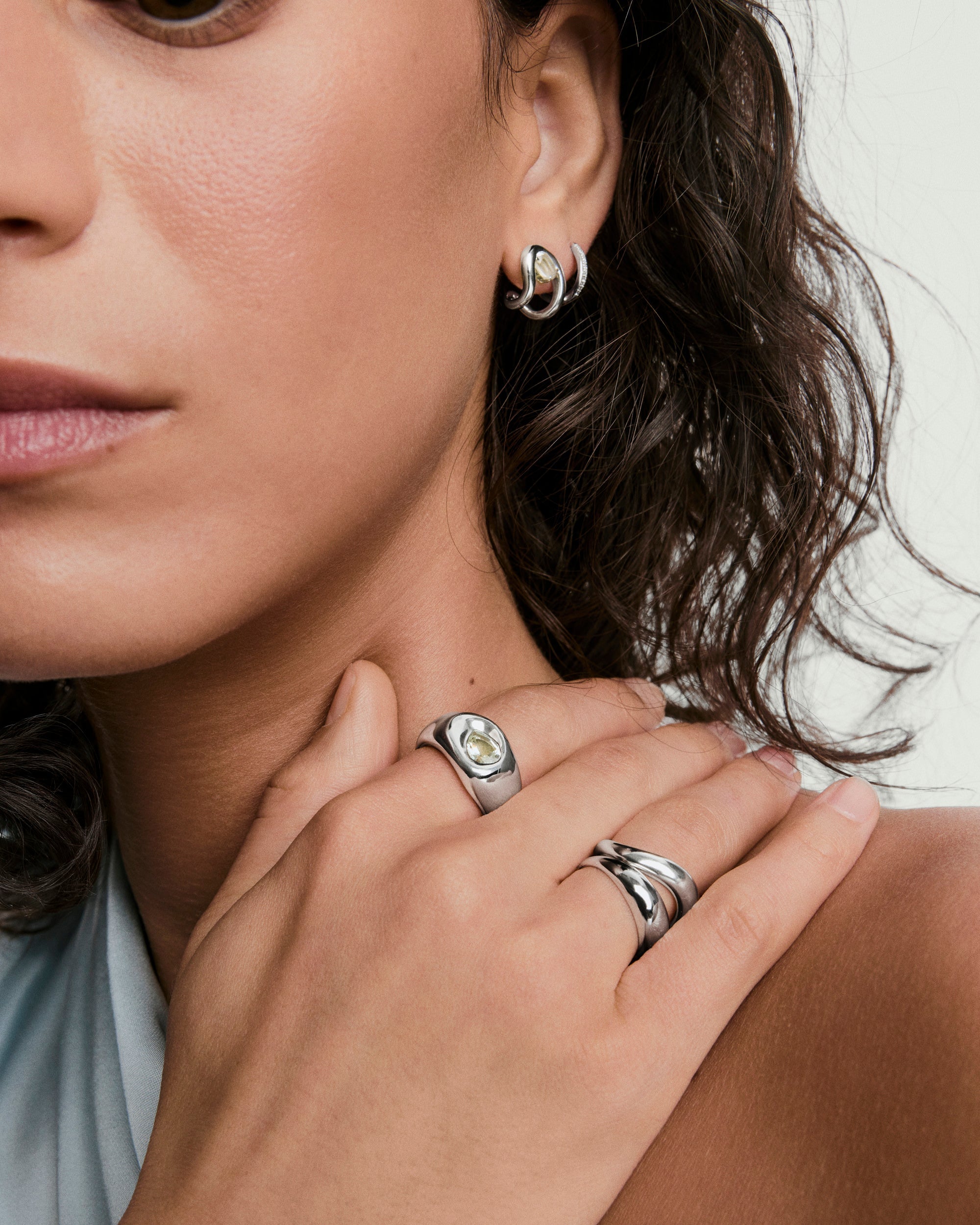 Organic DÃ´me Curve Gemstone Huggies showcased on a woman's ear, highlighting the elegant design with a gemstone embedded within the earring's open center.
