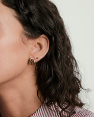 Organic DÃ´me Curve Gemstone Huggies showcased on a woman's ear, featuring a central red stone, highlighting the earring's artistic and unique design.