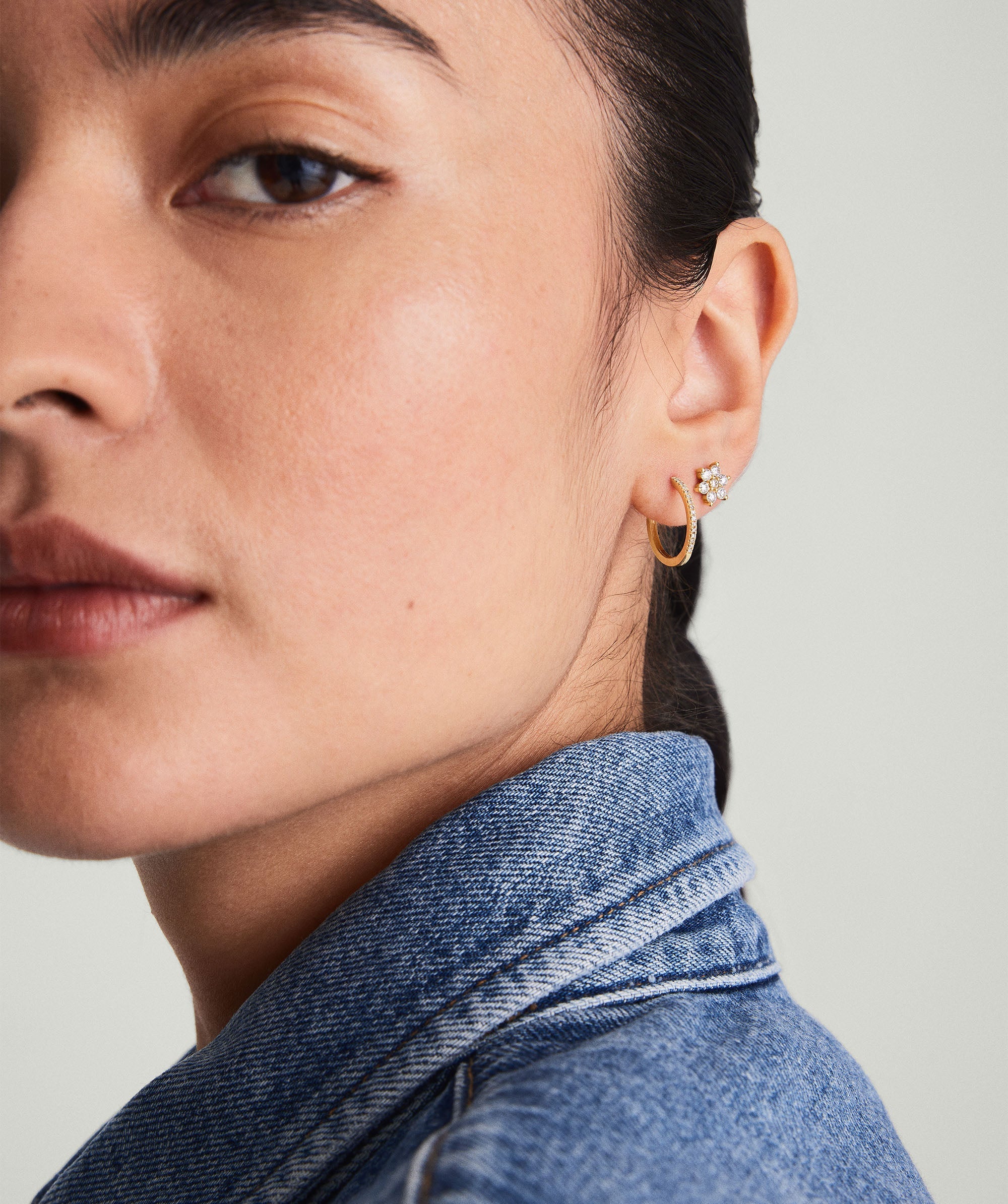 Close-up of a woman's face showcasing PavÃ© Diamond Small Hoops, handcrafted in recycled 14k gold, worn on her ear.