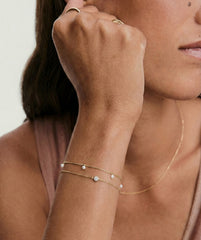 Light and Luster Bracelet Bundle: Two fine gold-chain bracelets, one with freshwater pearls, the other with a lab-grown sapphire, elegantly adorn a woman's wrist.