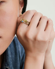 Close-up of a hand wearing the Bold Puzzle Stacking Ring, featuring three slim gold bands with pale blue, light green gemstones, and tiny accent diamonds.