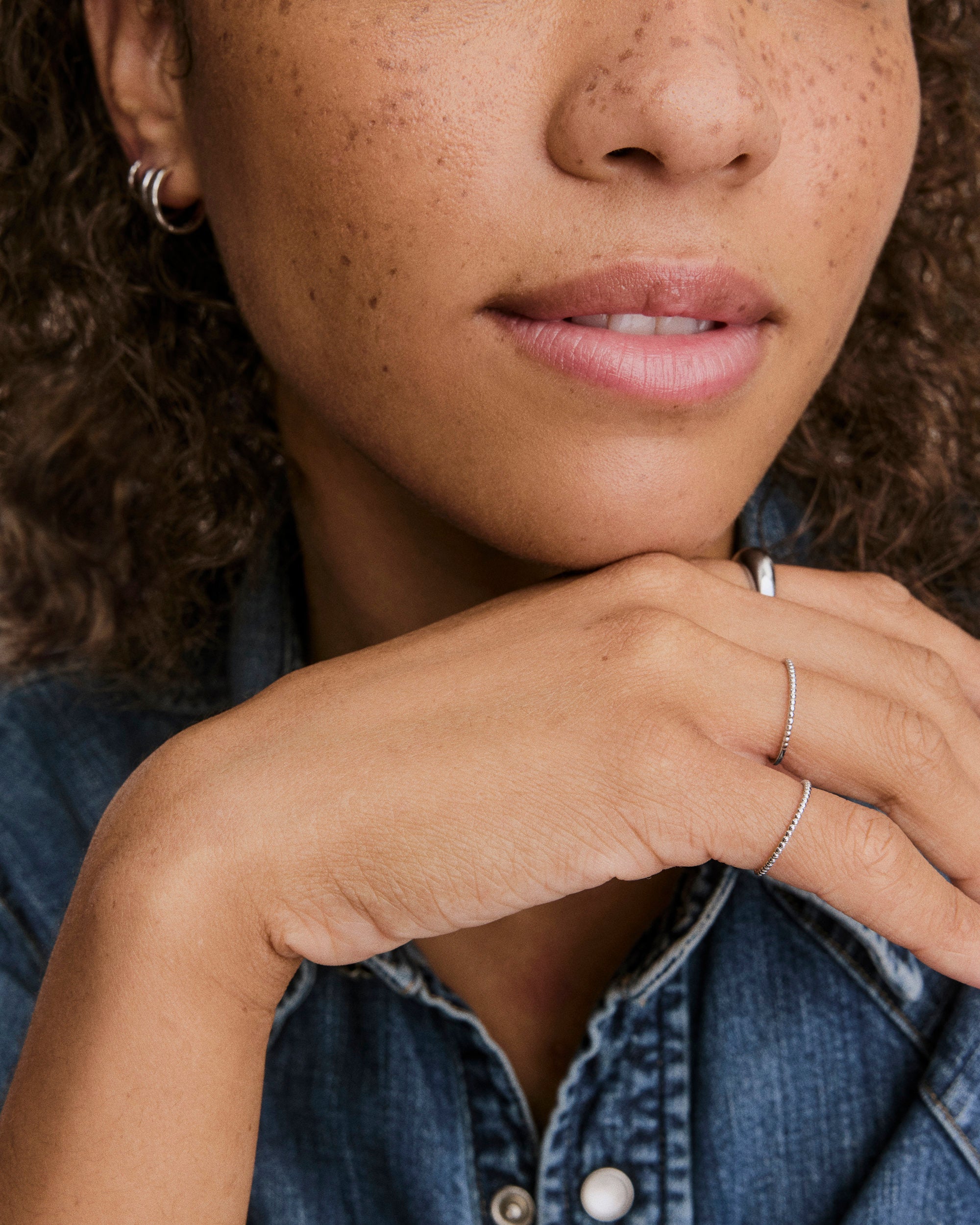 Close-up of a hand under the chin wearing the Beaded Ring, a delicate 1.3 mm silver band, alongside another thin ring.