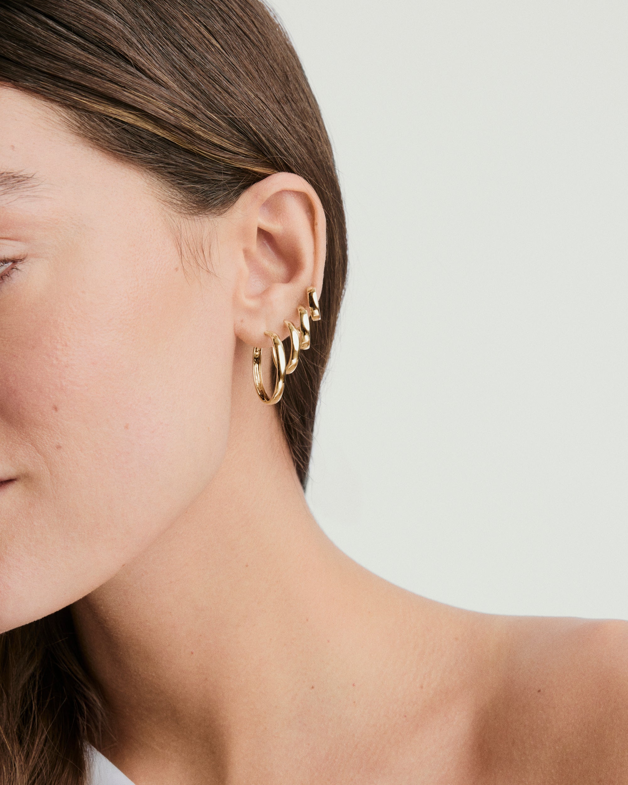 Close-up of a woman's ear adorned with Bold Large Hoops, showcasing handcrafted, recycled 14k solid gold earrings that elevate any outfit.