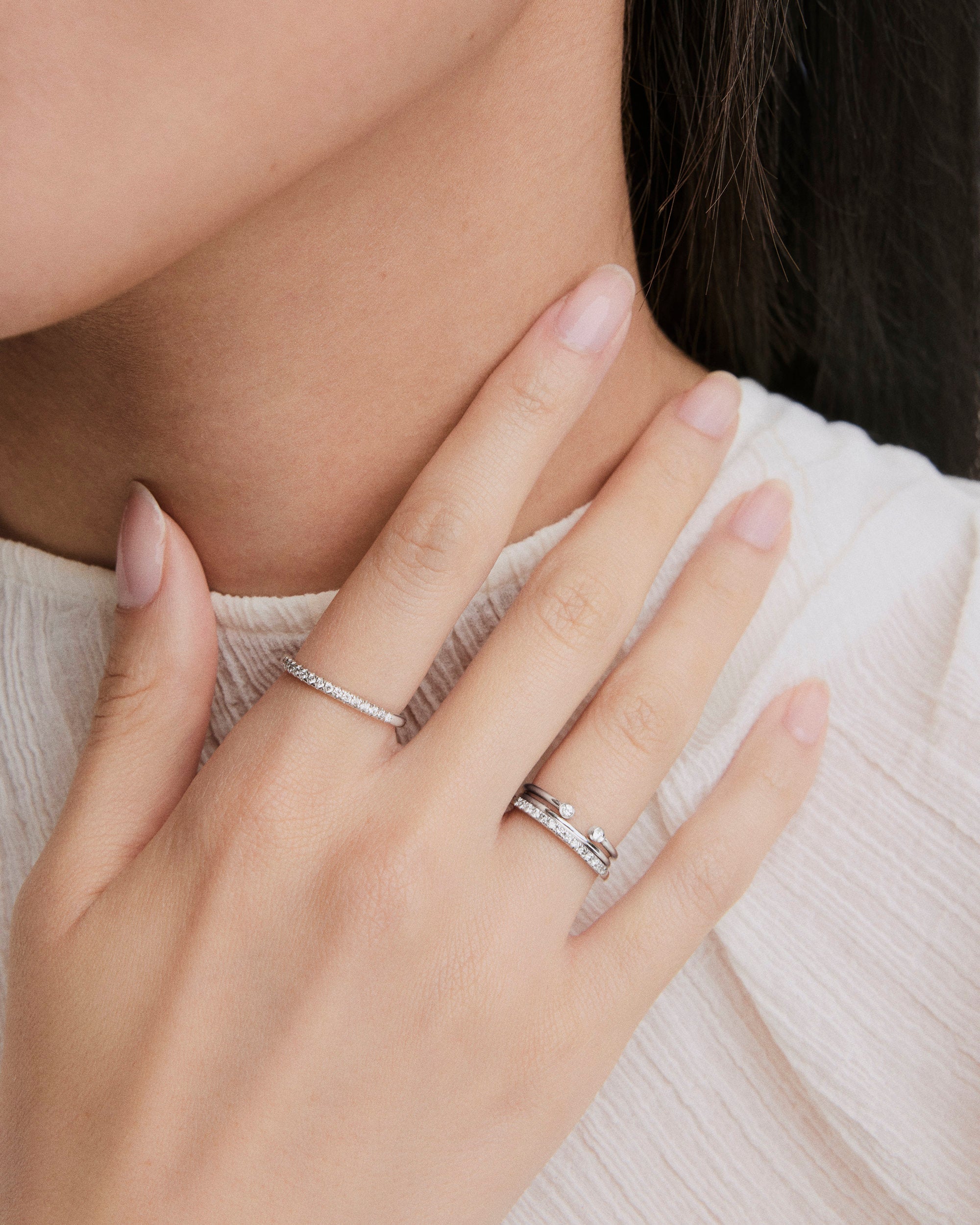 A hand wearing the Diamonds Team Ring, featuring two slim diamond-set bands and one polished band with small stones, against a light textured fabric background.
