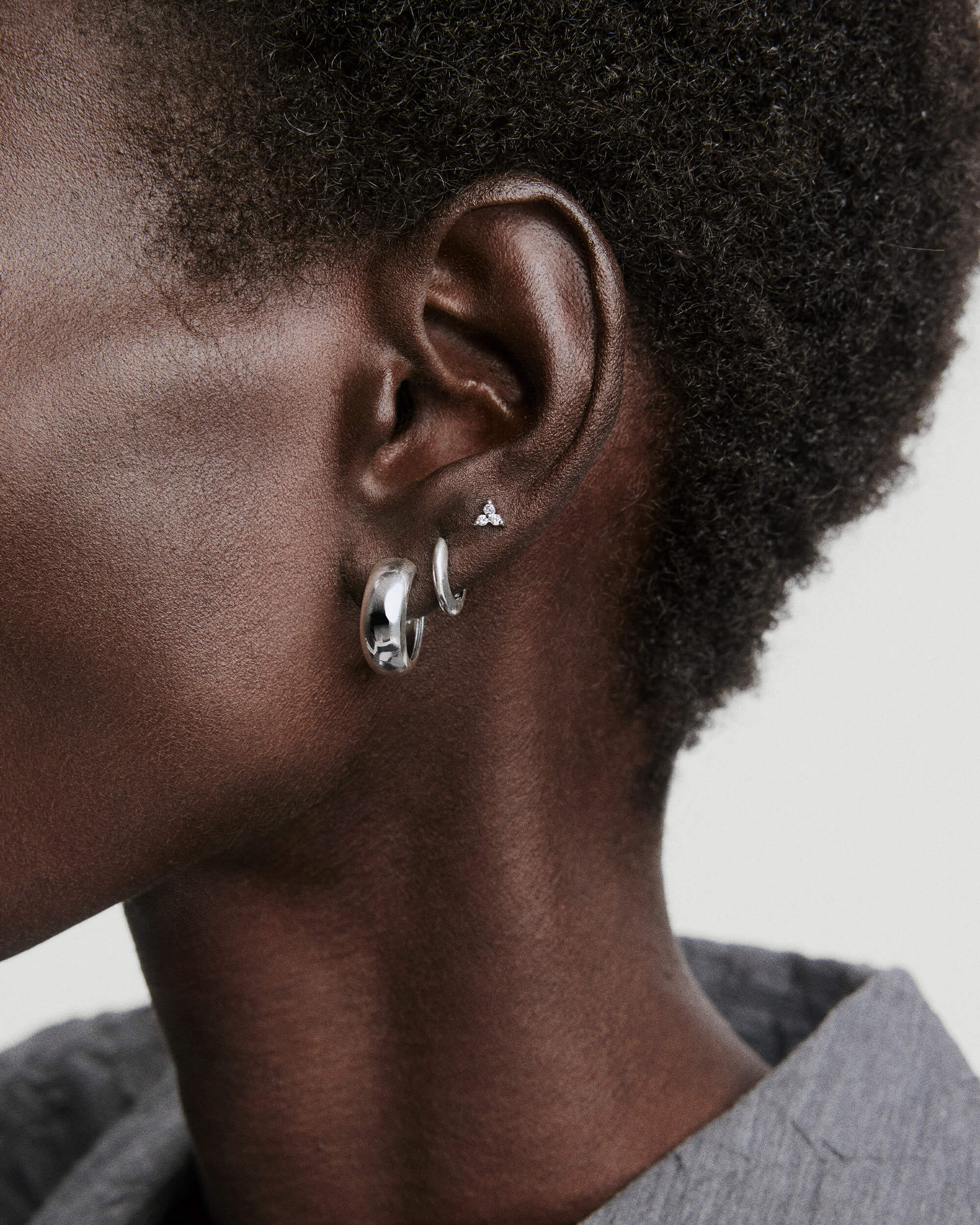 Close-up of an ear wearing three earrings, including the Mini Lotus Diamond Studs crafted in 14k gold with lotus-shaped diamonds, perfect for stacking.