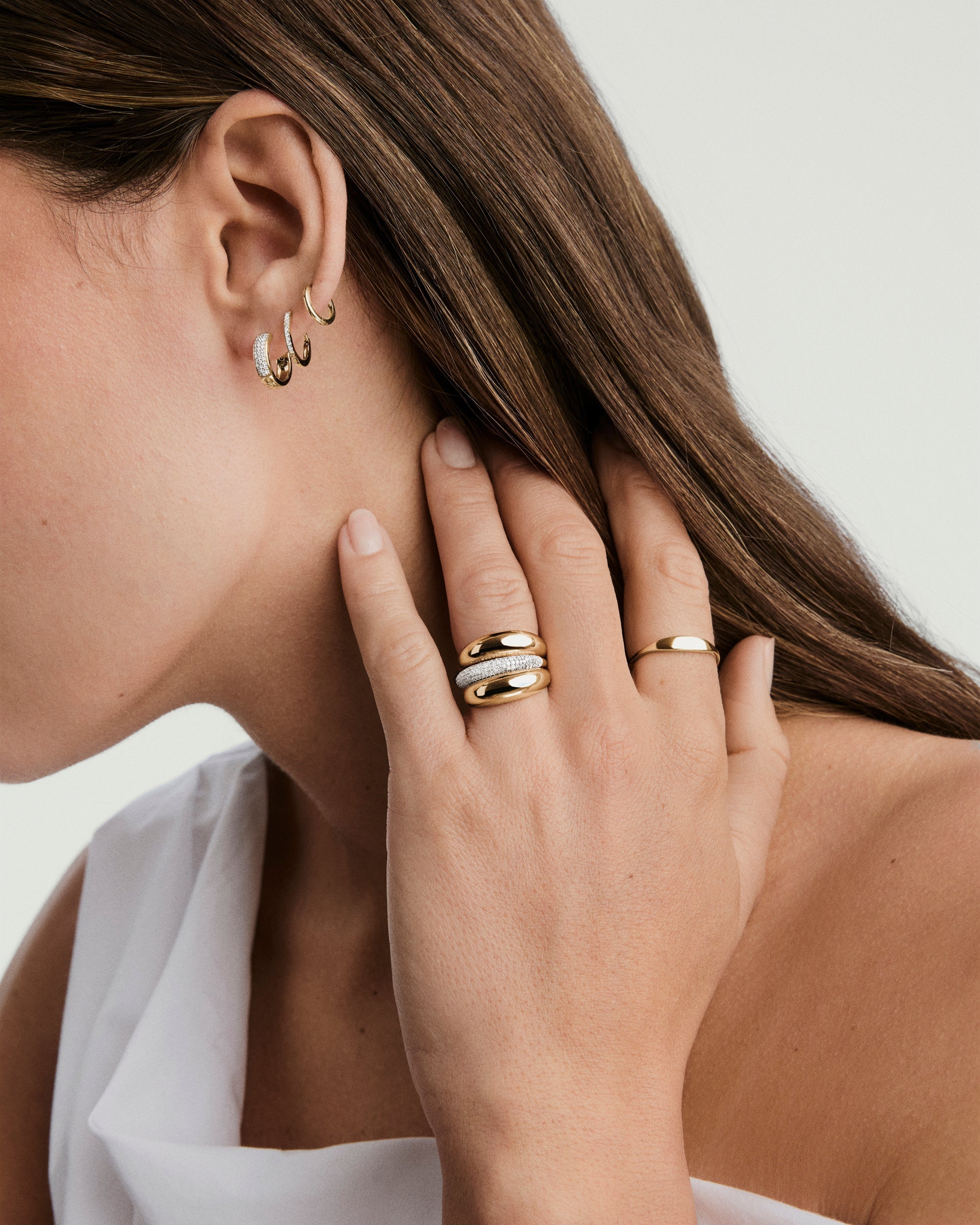 PavÃ© Diamond Huggie Hoops on a woman's ear, showcasing handcrafted 14k gold with pavÃ© diamonds, designed for versatile wear.