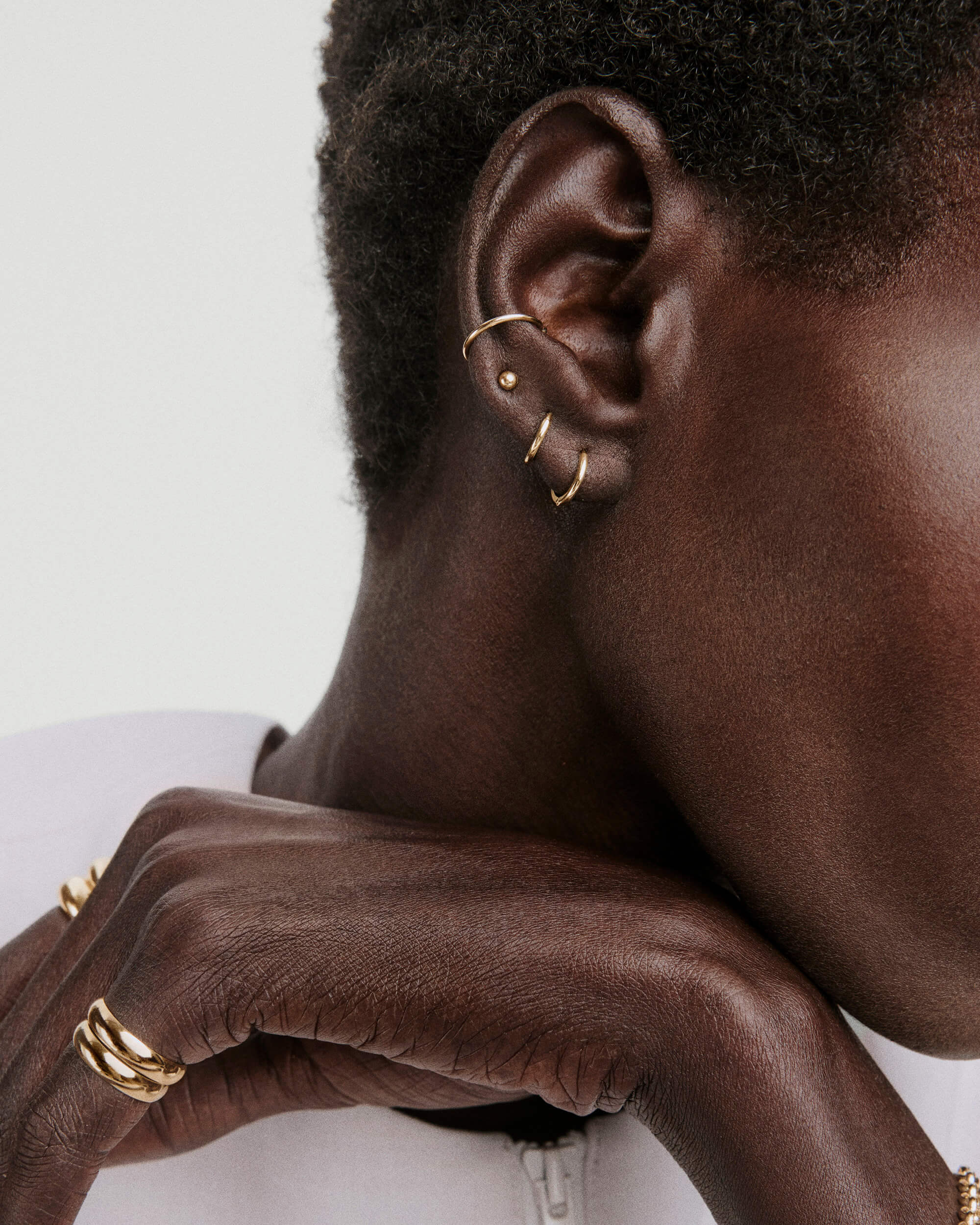 Sphere Studs worn on ear, complemented by three gold hoops. The hand displays chunky gold rings, enhancing the elegant, versatile look of the stud.