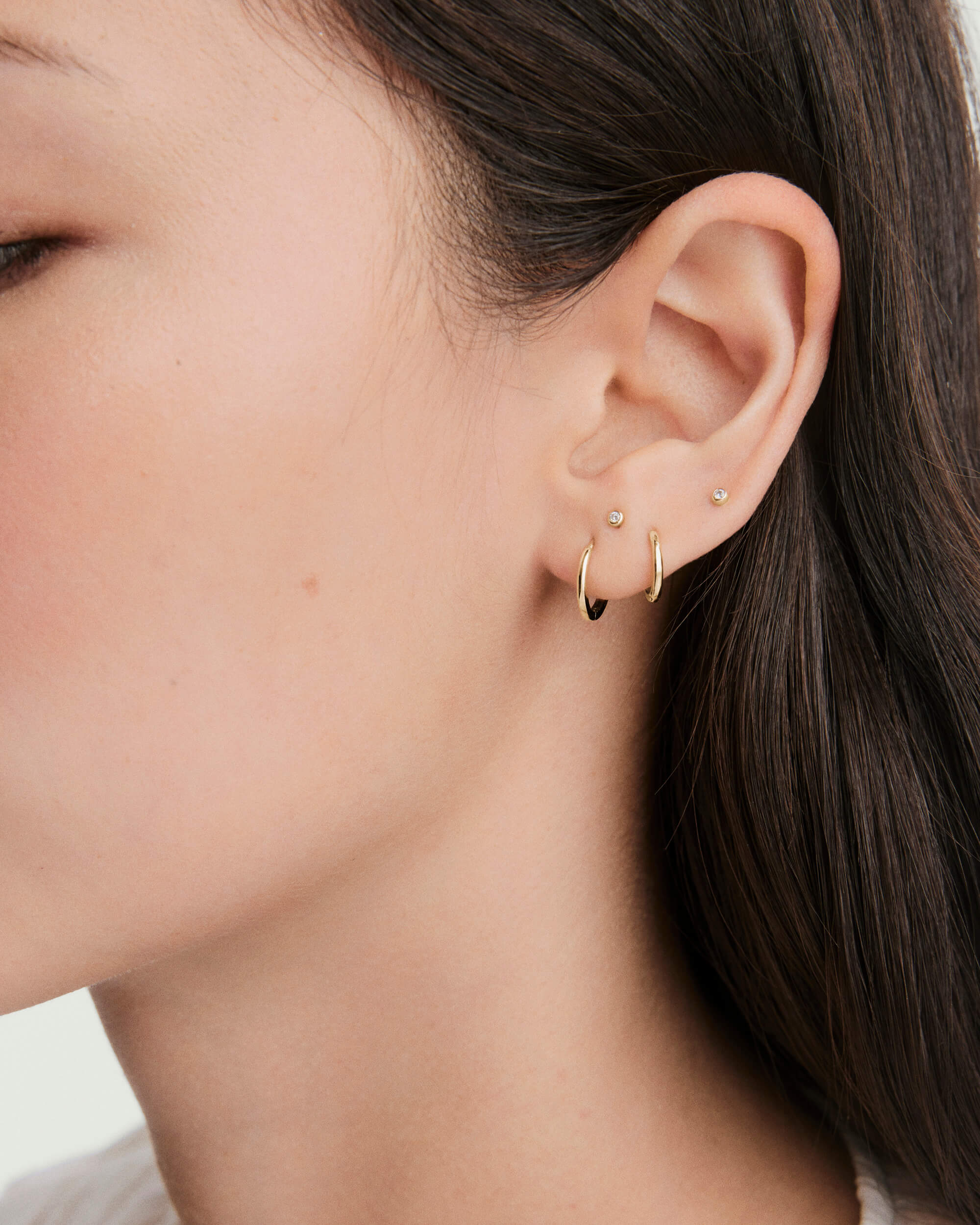 Close-up of a woman's ear wearing Tiny Diamond Studs in bezel settings, showcasing their miniature shine and flat back design for comfort.