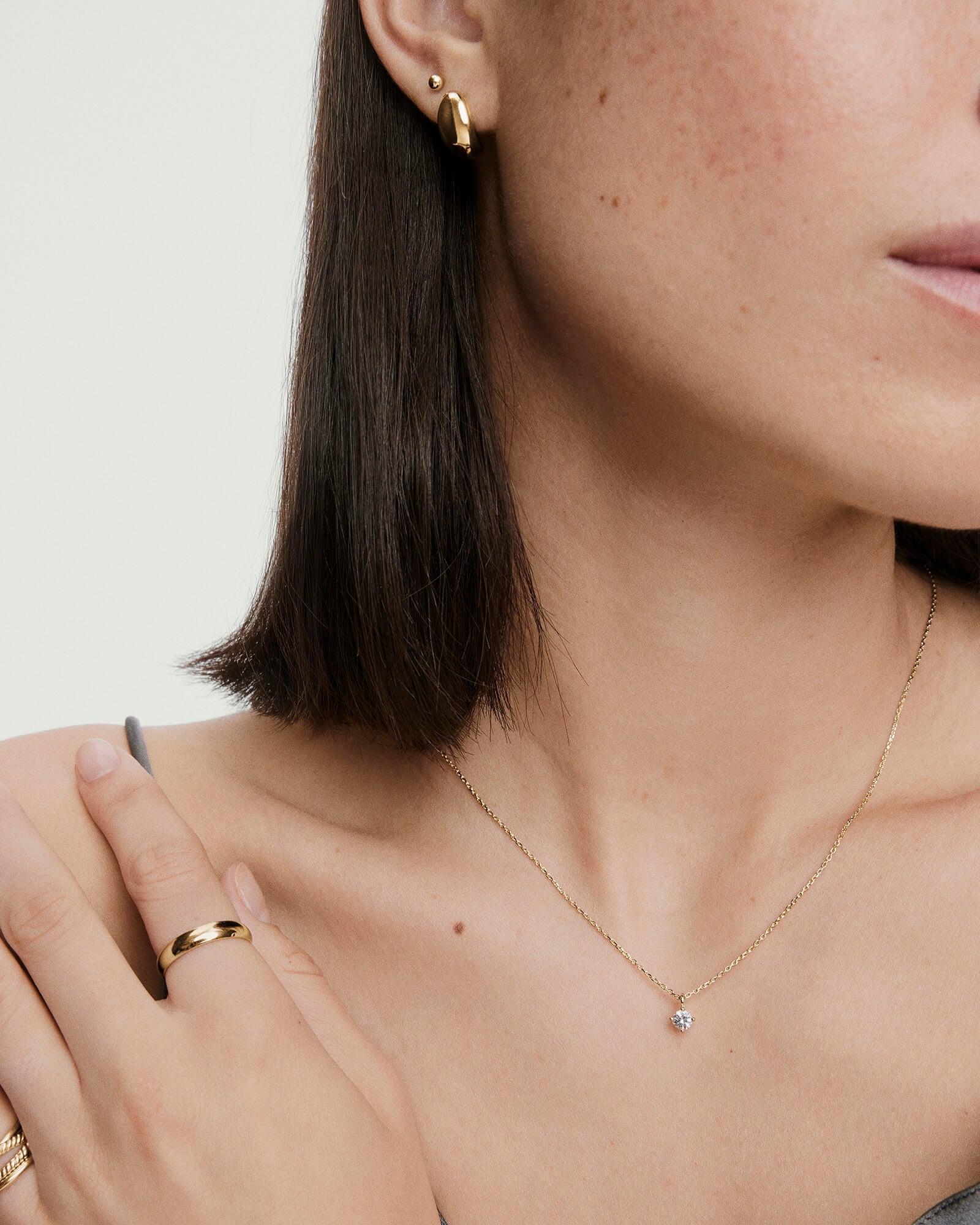 Woman wearing a Round Lab Grown Sapphire Necklace, featuring a gold chain and round pendant, complemented by gold earrings and rings, with a natural look.