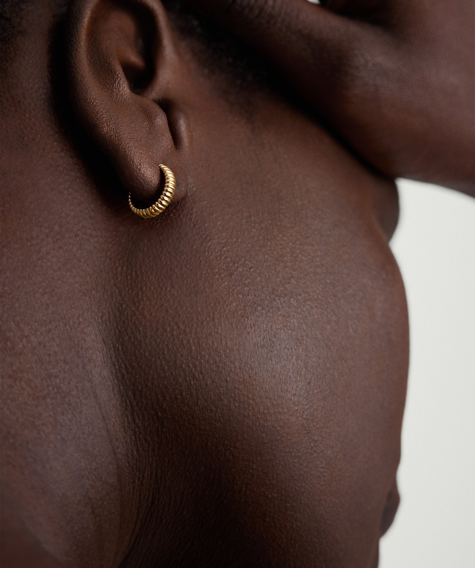 Close-up of a person's ear showcasing the Bold Micro Charlotte Huggie Hoop in Salmon Gold.