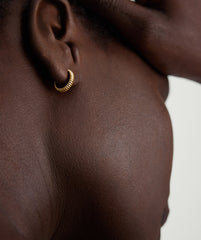 Close-up of a person's ear showcasing the Bold Micro Charlotte Huggie Hoop in Salmon Gold.