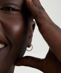 Close-up of a woman's ear wearing Bold Micro Charlotte Small Hoop Salmon Gold with a plissÃ© texture, highlighting the handcrafted design and statement-making style.