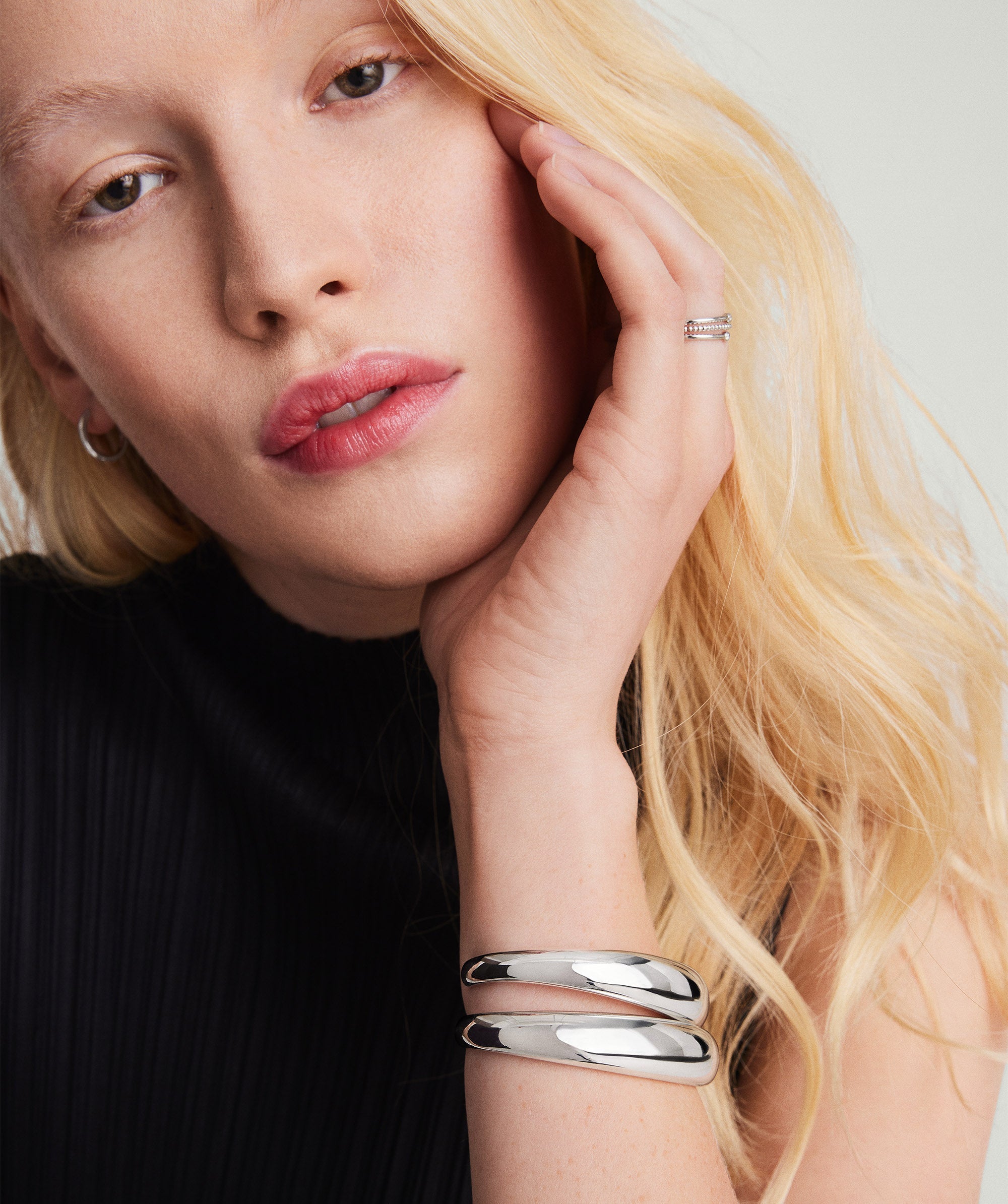 A woman wearing a black shirt showcases the 13mm DÃ´me Cuff Bracelet in handcrafted 925 sterling silver, paired with other silver jewelry.