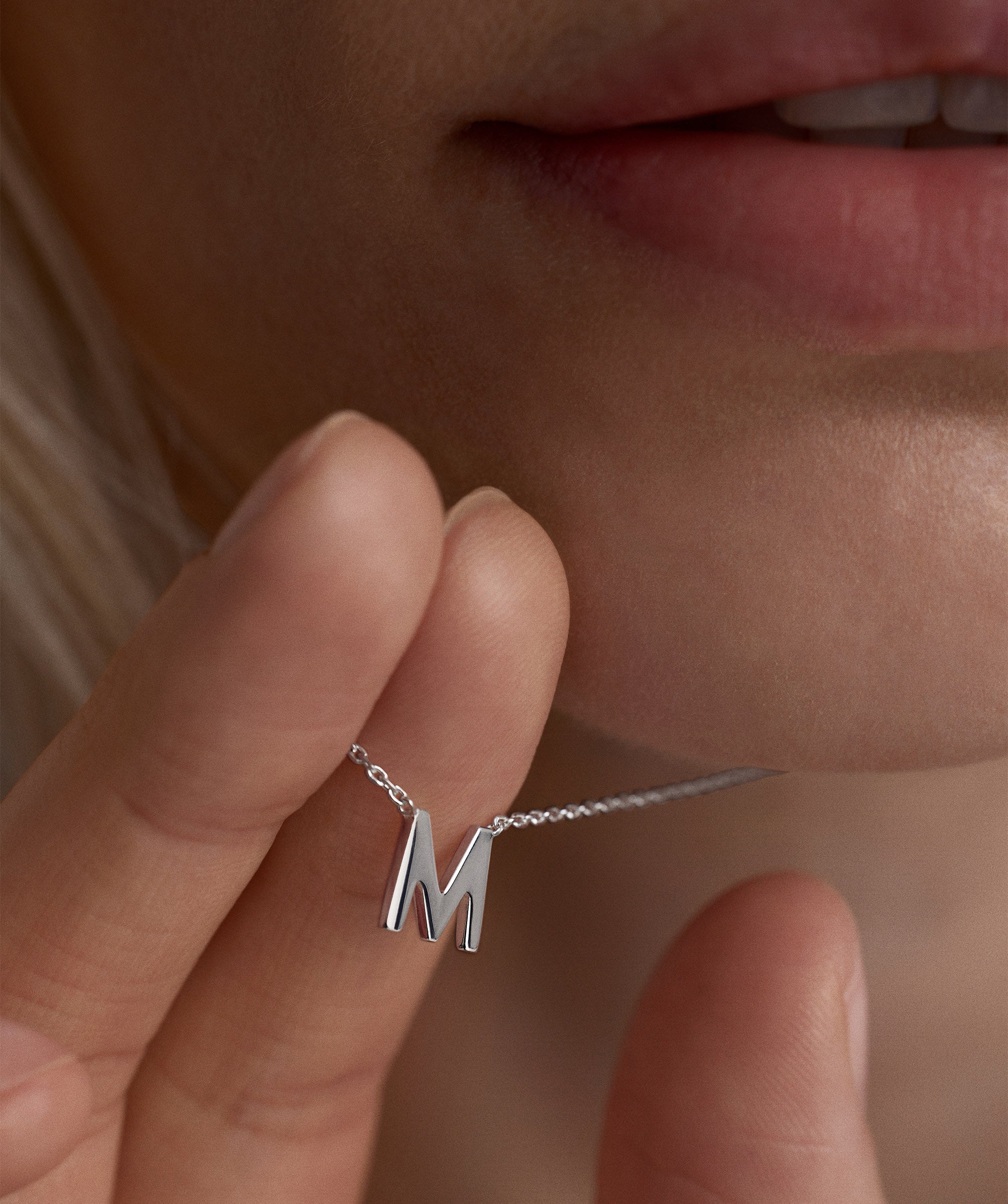 Person wearing a silver letter M necklace, showcasing its intricate chain and elegant design.