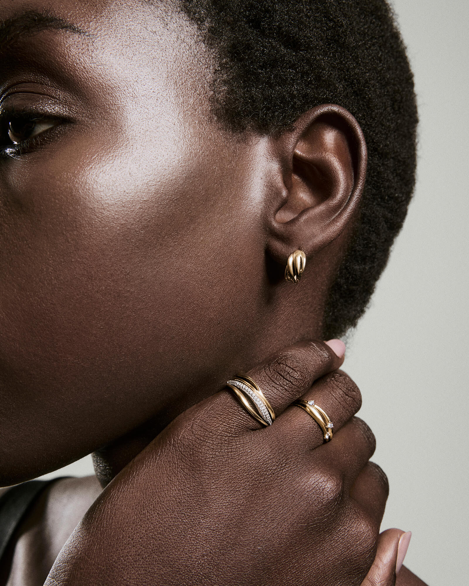 Close-up of a person's ear with Open DÃ´me Hoops, a small sculptural gold earring, paired with gold rings showcasing pavÃ© diamonds and a gemstone.