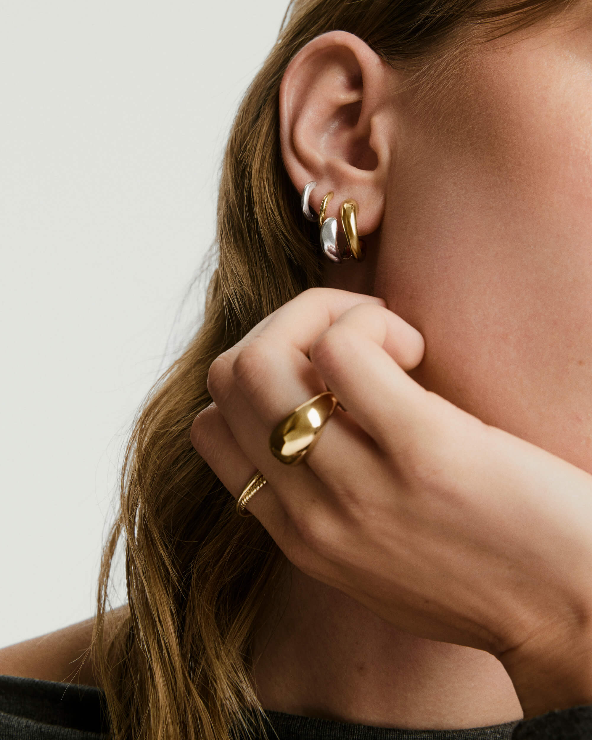 Jojo Double Hoops elegantly adorn a woman's ear, featuring a mixed metal design with an optical illusion, emphasizing fashionable jewelry style.