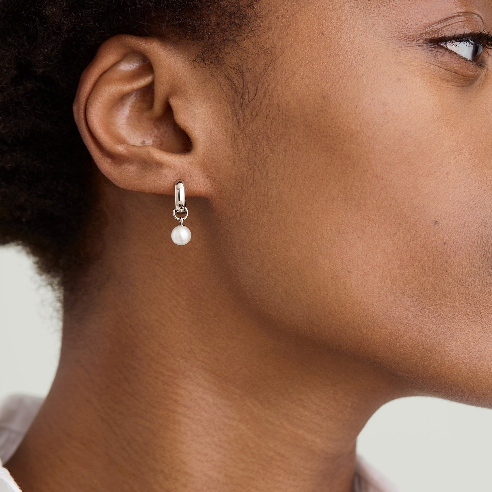 Close-up of a woman's ear wearing a hoop earring with a single pearl charm, highlighting the earring's elegant and customizable design.
