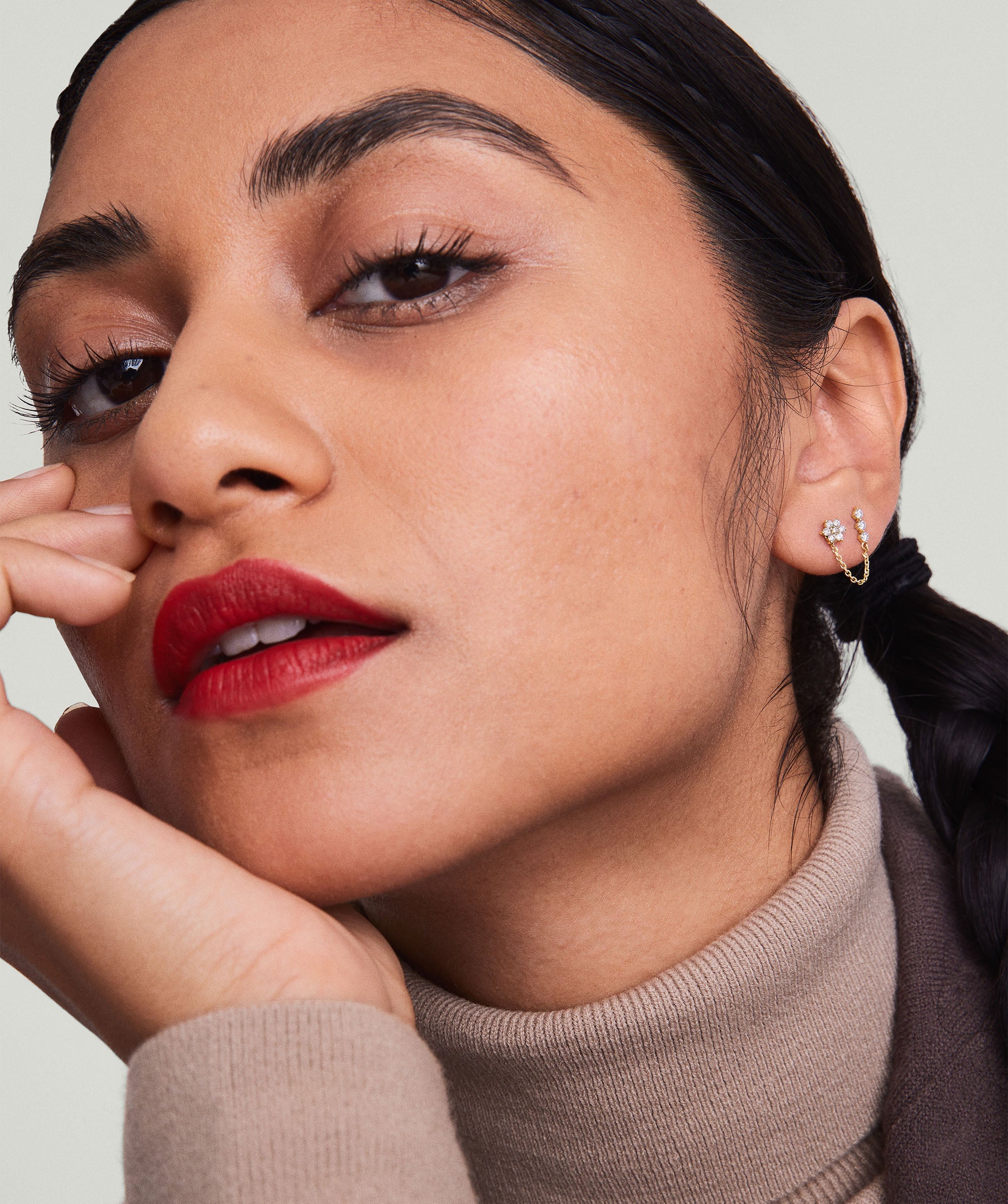 A woman wearing a Single Diamond Trio Chain Stud earring in 14k gold, featuring three diamonds, with her hand gently touching her face.