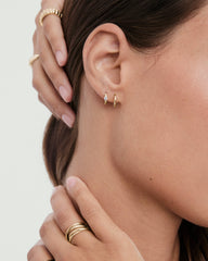Woman wearing two gold hoops, one being the Single Colored Mini Hoop with a clear stone, showcasing its delicate design alongside slender gold rings on her fingers.