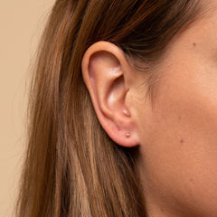 Close-up of a woman's ear wearing Sphere Studs, small round earrings ideal as starter studs, highlighting their simple elegance and versatility for everyday wear.