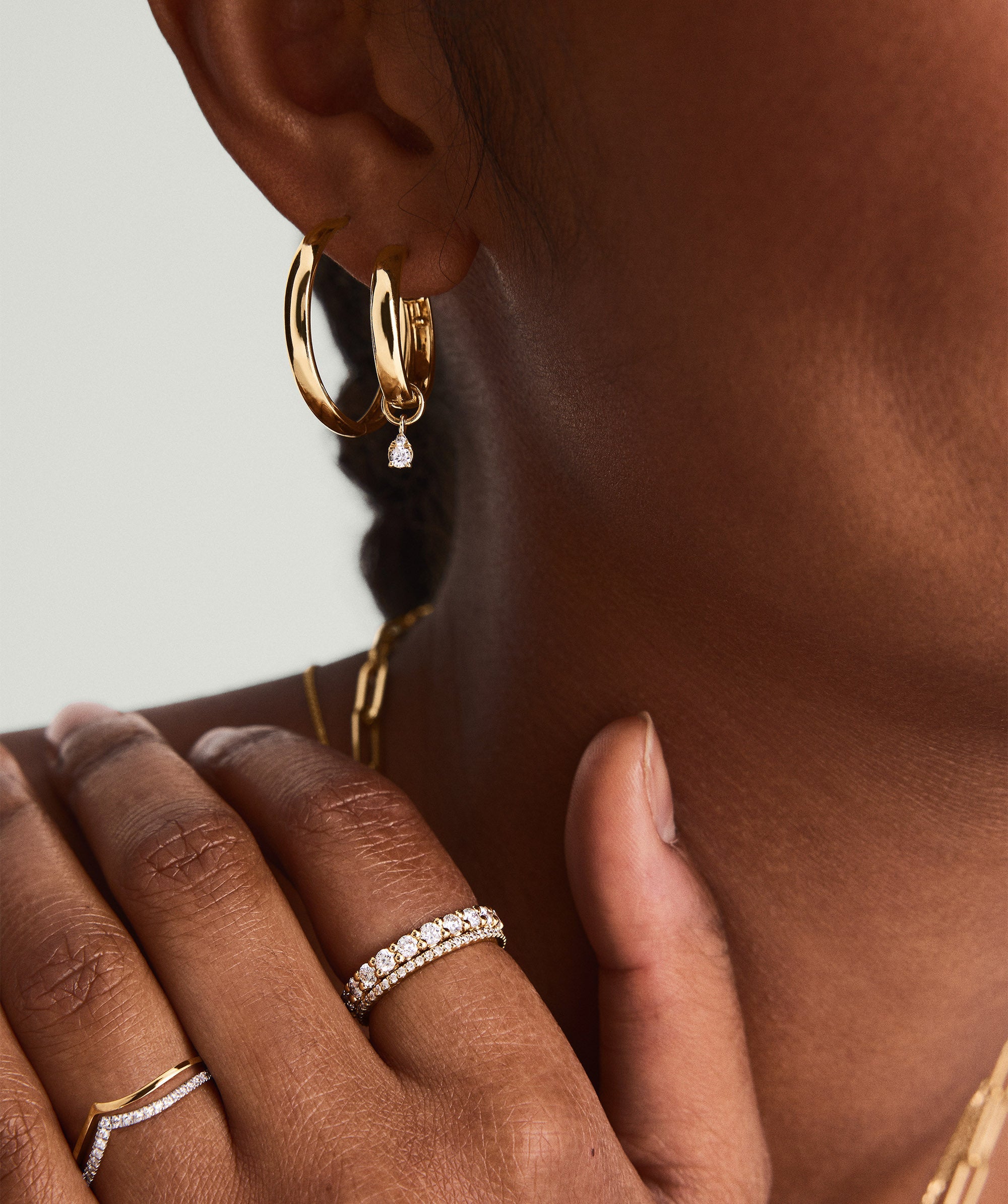 Close-up of a woman's ear adorned with a Mini Pear Diamond Hoop Charm in 14k solid gold, featuring a pear-shaped diamond.